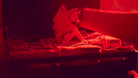 hombre con la mano tomando dinero del maletín con luz de fondo roja. maleta llena de dinero