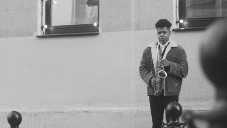 Blanco-Y-Negro-De-Un-Hombre-Con-Chaqueta-Tocando-El-Saxofón-En-La-Calle