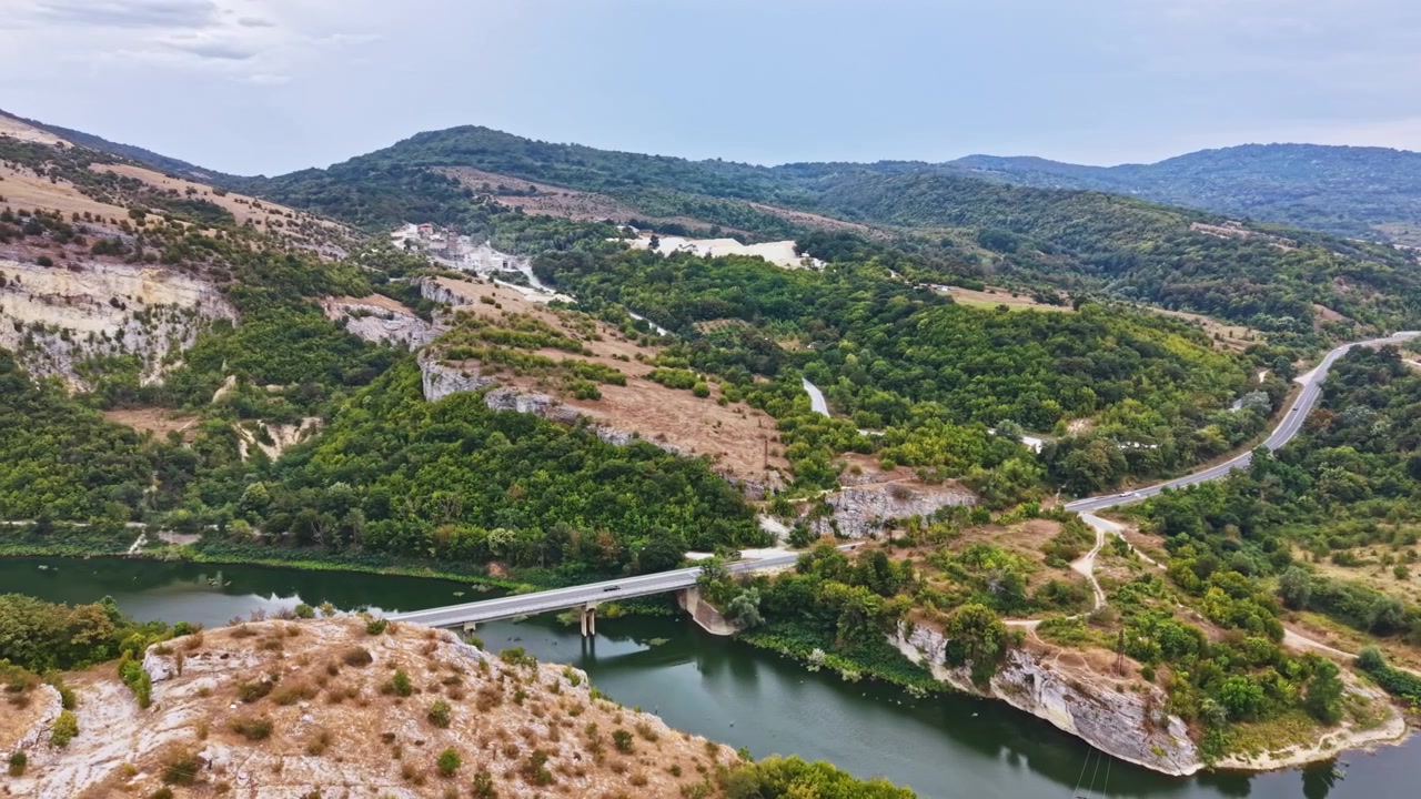 Vista panorámica de un río cruzando un puente rodeado de colinas y vegetación en una zona rural.