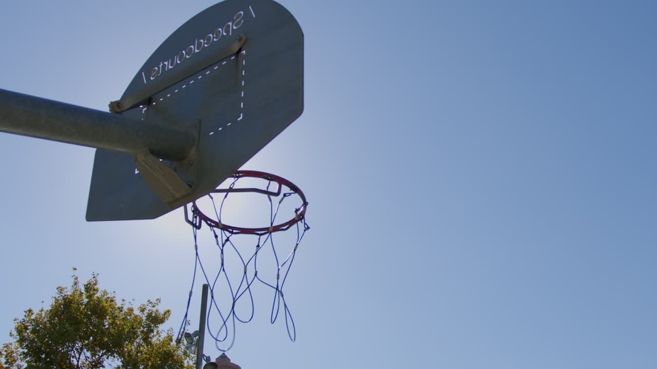 tiro medio de cámara lenta de una pelota de baloncesto haciendo una canasta en una cancha de baloncesto de la calle con una bengala en un día soleado