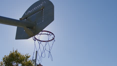 slow motion medium shot of a basketball making a basket on a street basketball court with a flare on a sunny day