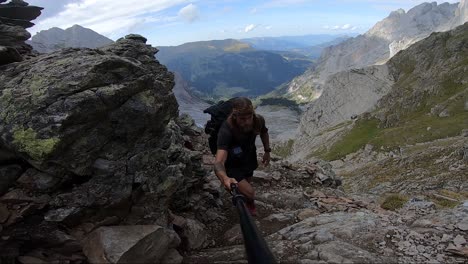 Un-Hombre-Joven,-Fuerte-Y-En-Forma-Con-Cabello-Largo-Y-Tatuajes-Camina-Por-Un-Sendero-De-Tierra-Empinado-En-Suiza-Durante-Un-Día-De-Verano