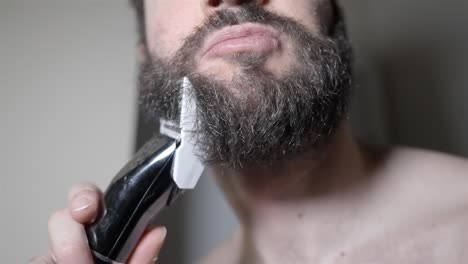 man trimming beard cheek line with electric shaver, detailed slow motion