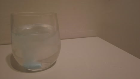 Blue-pill-thrown-to-a-glass-of-water-with-a-white-background-wall,-producing-a-effervescence-effect