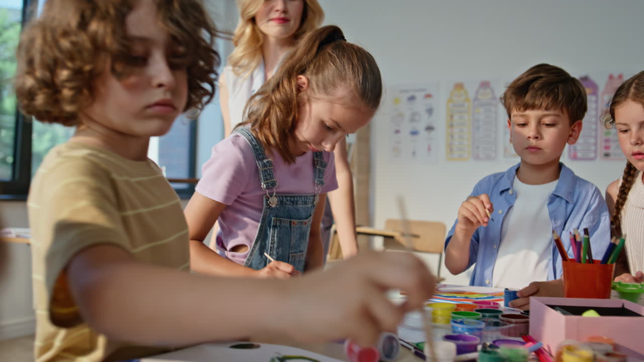 Art teacher helping children at creative lesson in bright classroom closeup