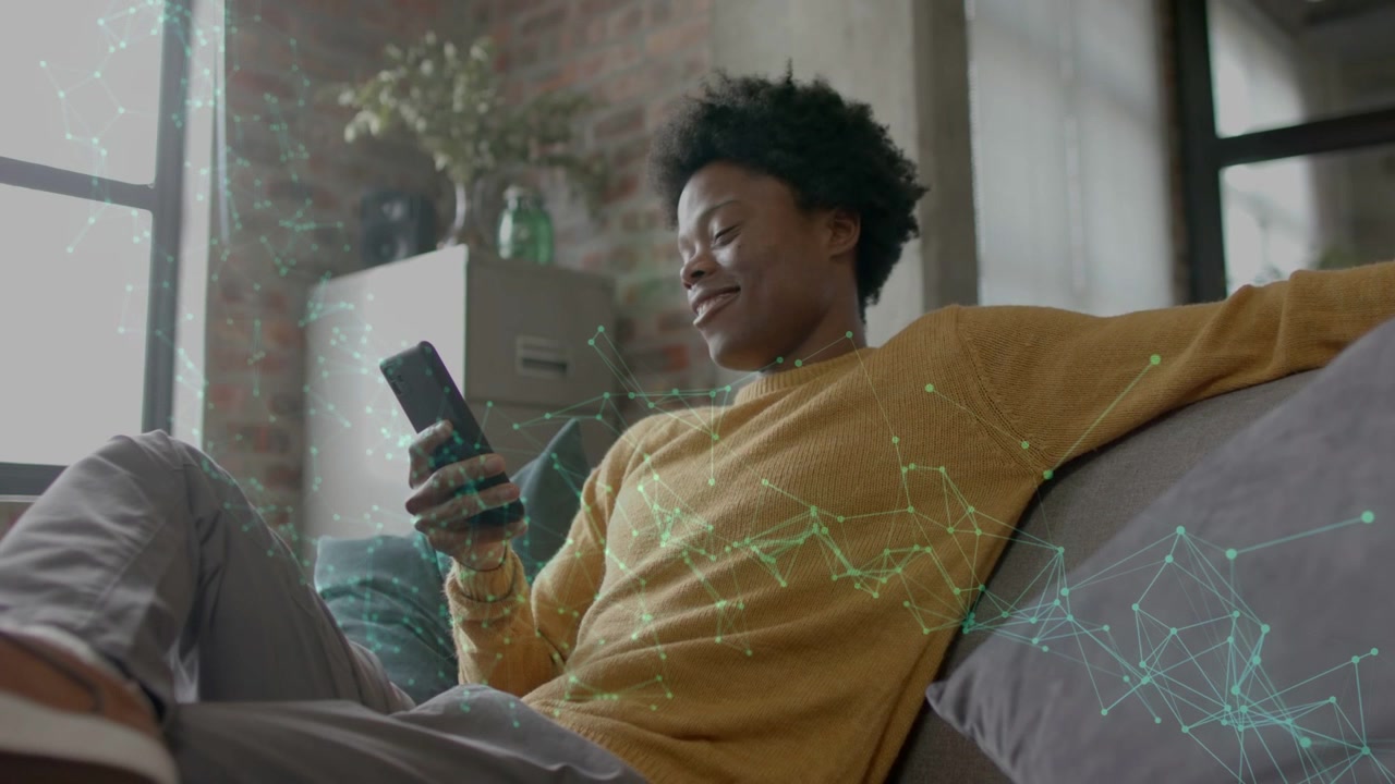 Man raising smartphone and scrolling on couch, green tech overlay appearing across frame, relaxing
