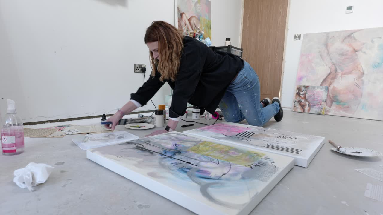 Female artist on floor of a busy home studio, preparing to paint a canvas