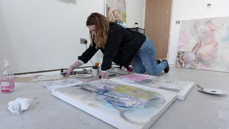 female artist on floor of a busy home studio, preparing to paint a canvas