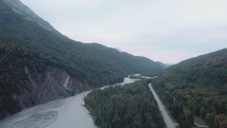 Aerial-view,-drone-flight-along-the-Glenn-Highway-and-the-Matanuska-River-in-the-Chugach-Mountain-Range-of-central-Alaska-on-a-cloudy-summer-day