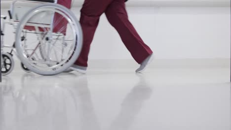 african american female doctor running with wheelchair in hospital corridor, slow motion