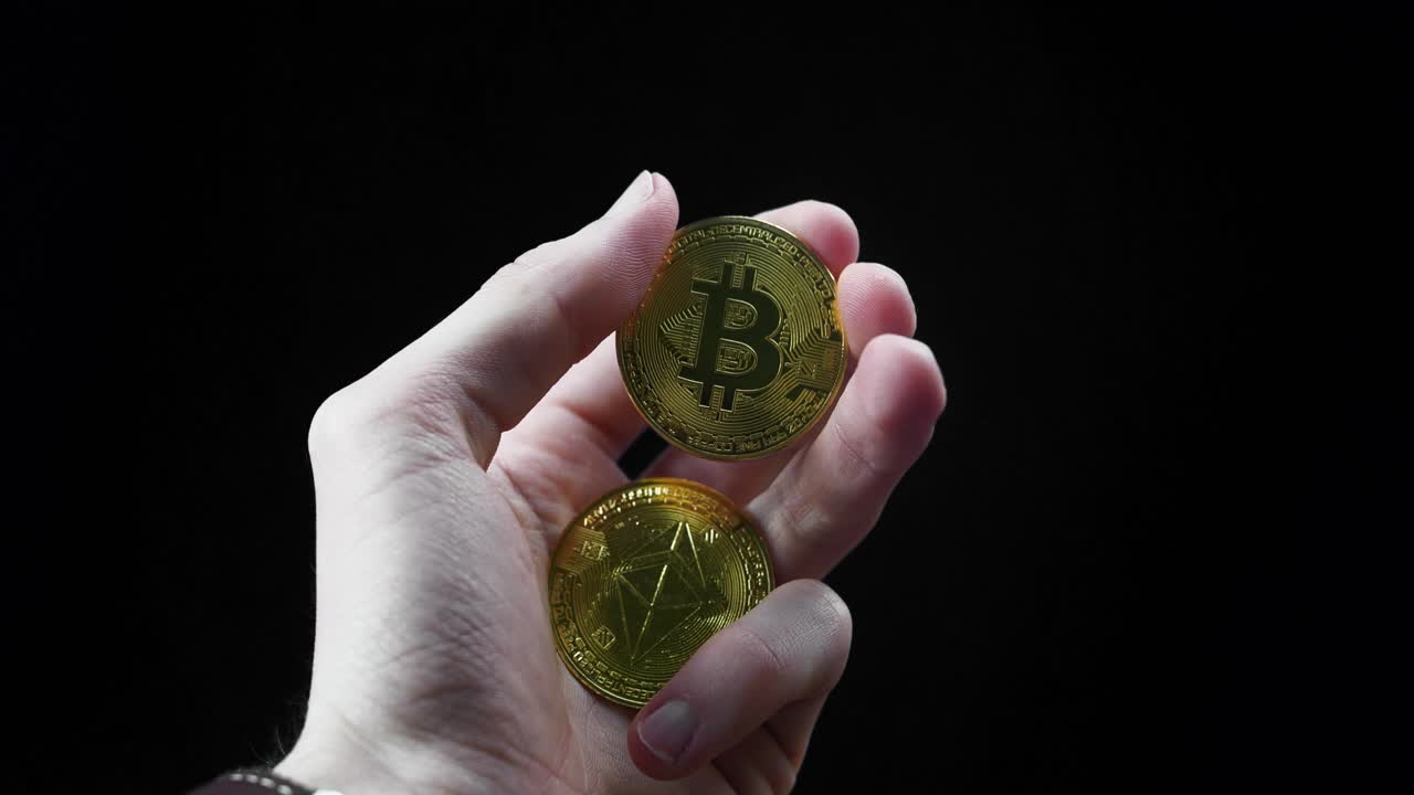 Hand holding shiny golden Ethereum coin and Bitcoin in a studio