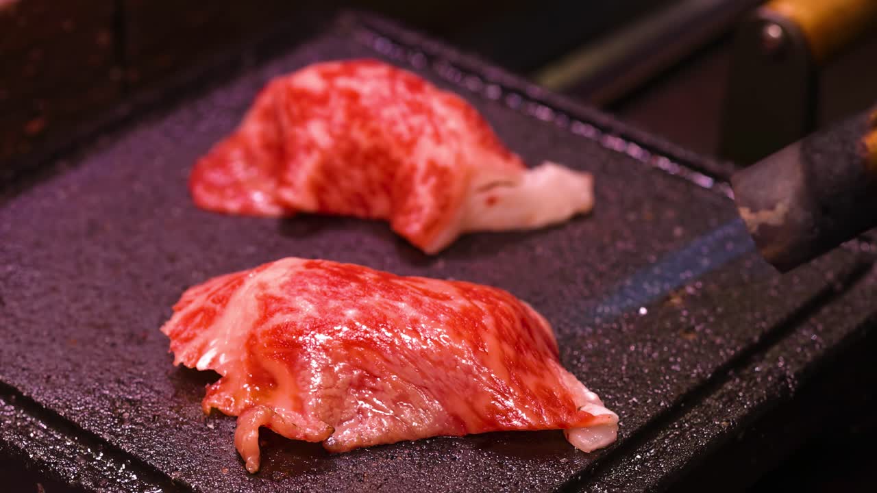 Detailed view of marbled beef slices cooking on a hot griddle, highlighting texture and searing process.