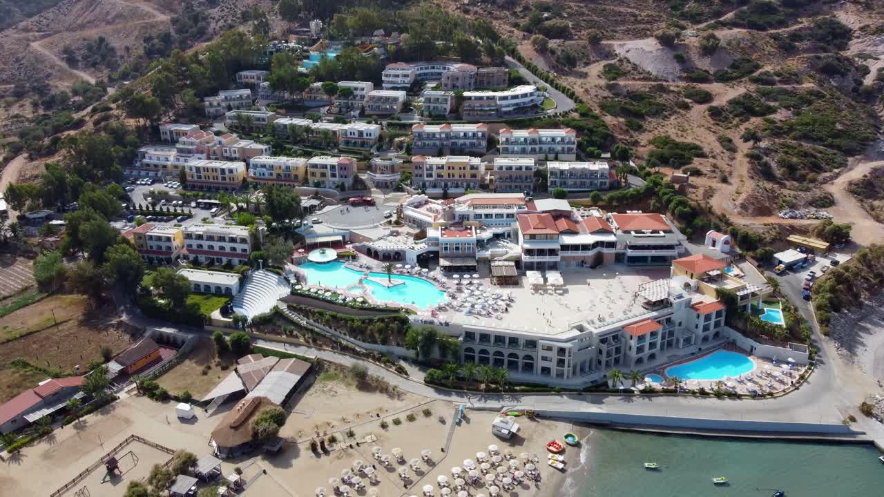 드론은 그리스 크레타의 해변을 날아다니며 수영장과 워터 파크가 있는 휴양지 쪽으로 향합니다.