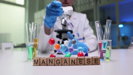 scientist working in a lab with microscope, test tubes, and 'manganese' spelled out on blocks