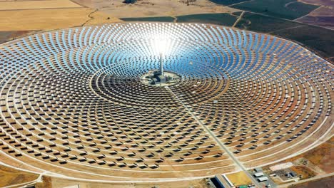 large circular power plant of solar panels in spain. there is the reflection of the sun in the the panels which produce renewable energy, solar energy - aerial view with a drone - environment concept