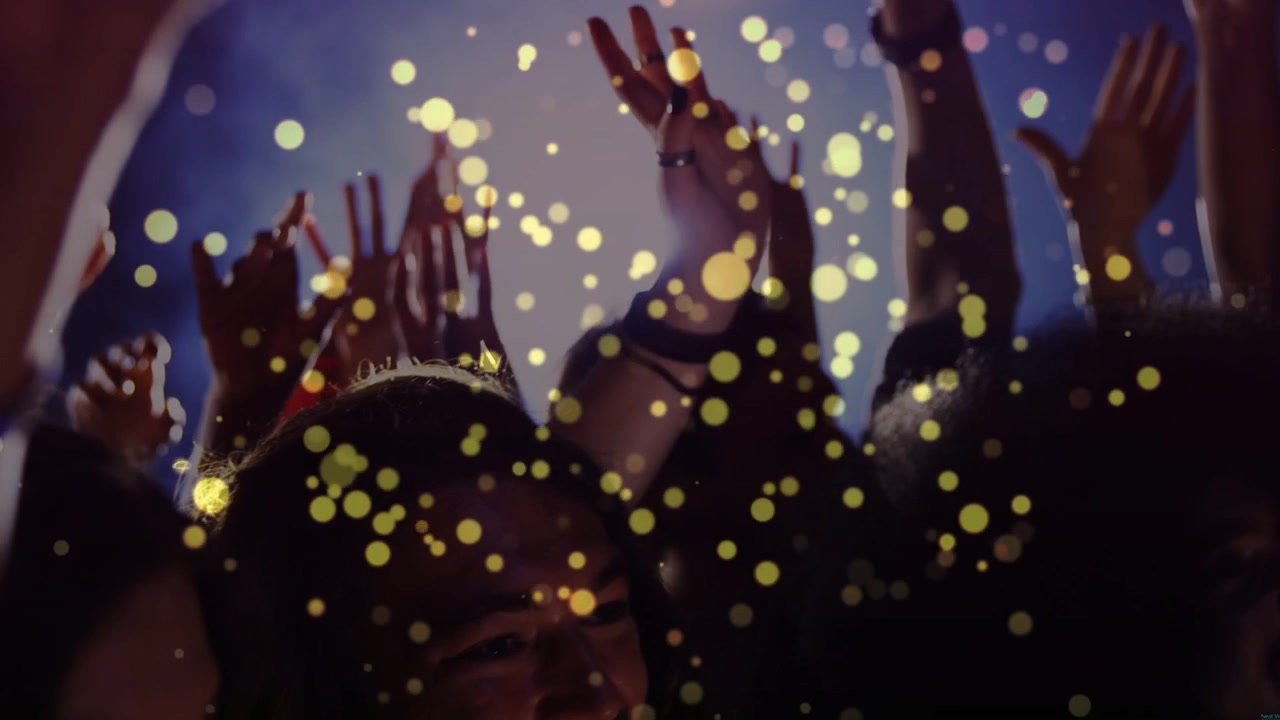 Folla del concerto che esulta, alzando le mani contro il controluce mentre particelle dorate fluttuano, rivelando le band