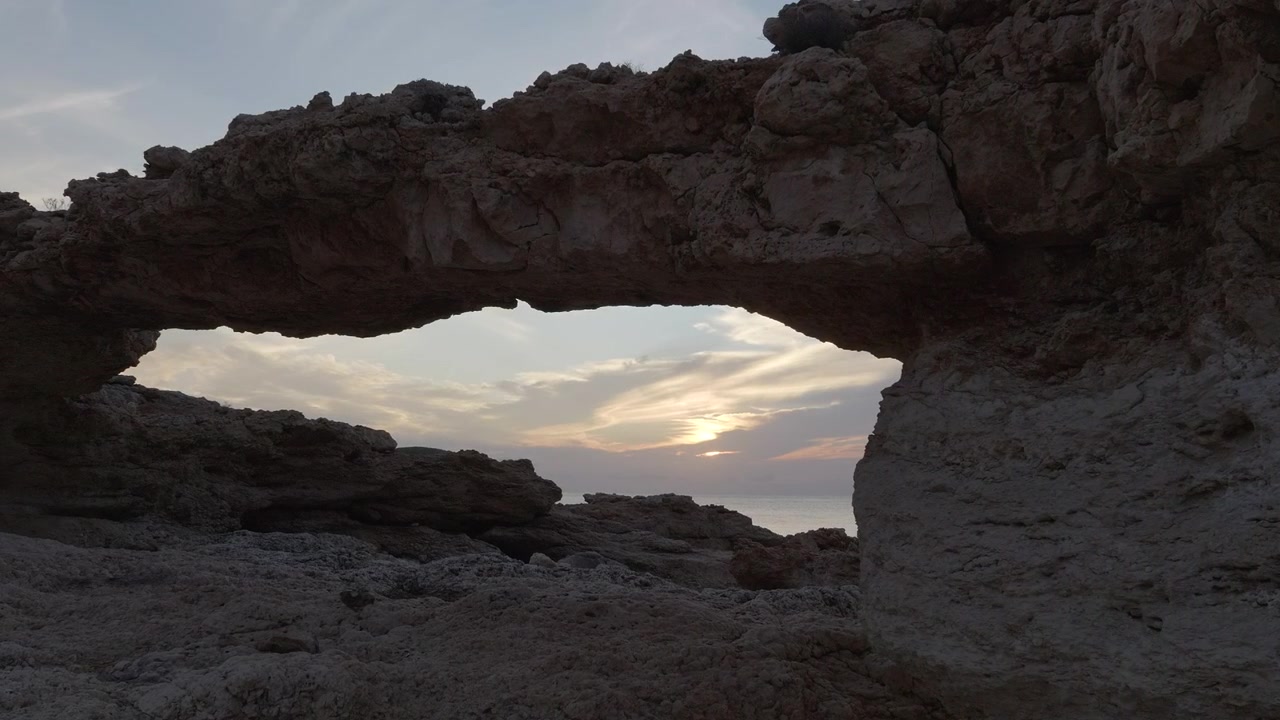 Admiring sunset between rock formations of deserted beach. Aerial, pan left