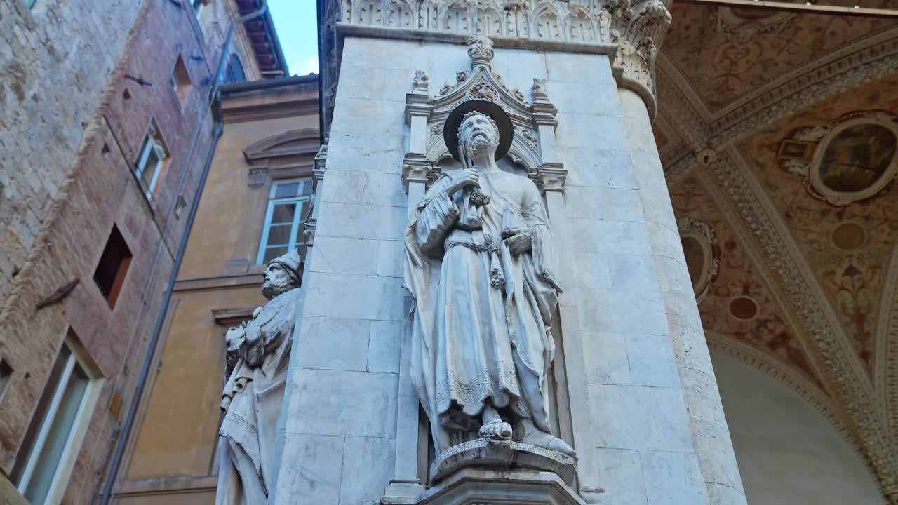 una estatua adorna un pilar de la logia de los comerciantes, loggia della mercanzia ubicada detrás de la plaza del campo, en siena, italia
