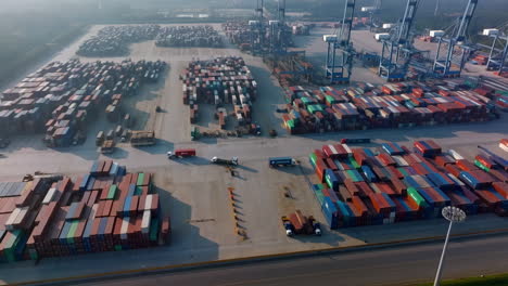 aerial view of a bustling container terminal at a shipping port with numerous cargo containers and cranes. a few trucks are seen transporting containers. a large industrial scene with a focus on global trade and logistics