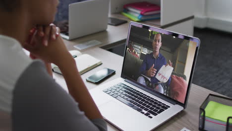 sección media de una mujer afroamericana haciendo una videollamada con un colega masculino en una computadora portátil en la oficina