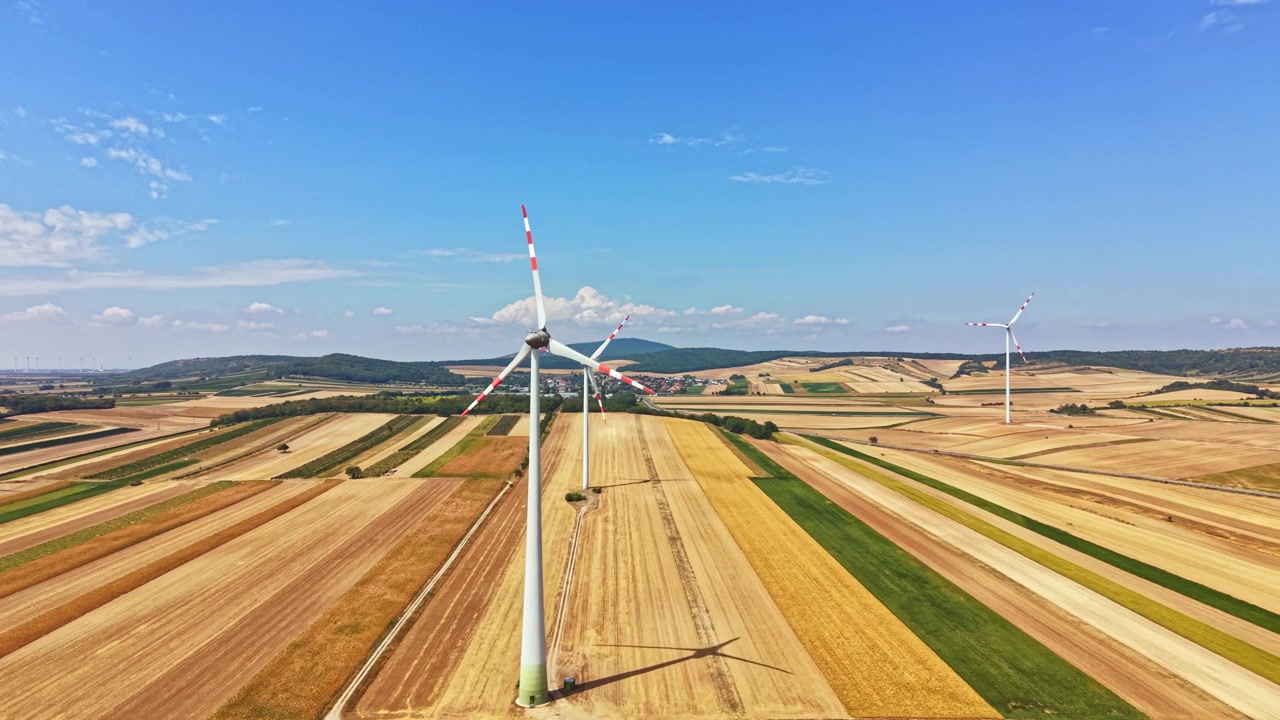 Wind turbines stand tall on fields under a blue sky with some clouds in a rural area during daytime