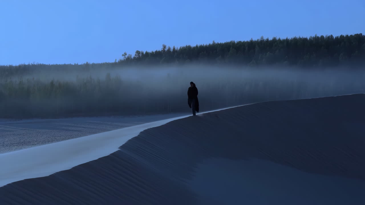 Solitary Figure on a Sand Dune with Misty Forest