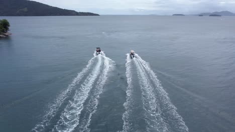 aerial view following two boats driving on the coast of ilha grande, cloudy brazil