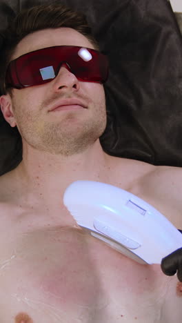 muscular caucasian man wearing protective goggles. male client undergoes the laser hair removal procedure. top view. vertical video