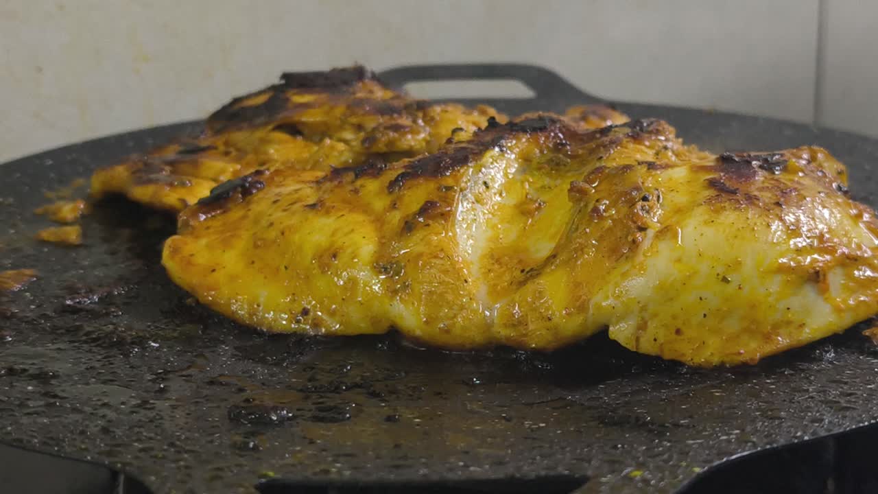 Chicken meat, marinated with spices, is grilled on a flat, non-stick pan. The spices sizzle, releasing a delicious aroma. Close-up shot shows the chicken browning perfectly on the grill