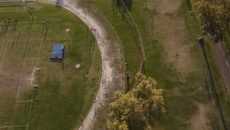 Aerial-top-down-shot-of-group-of-athletes-running-around-field-during-training-on-grass-court