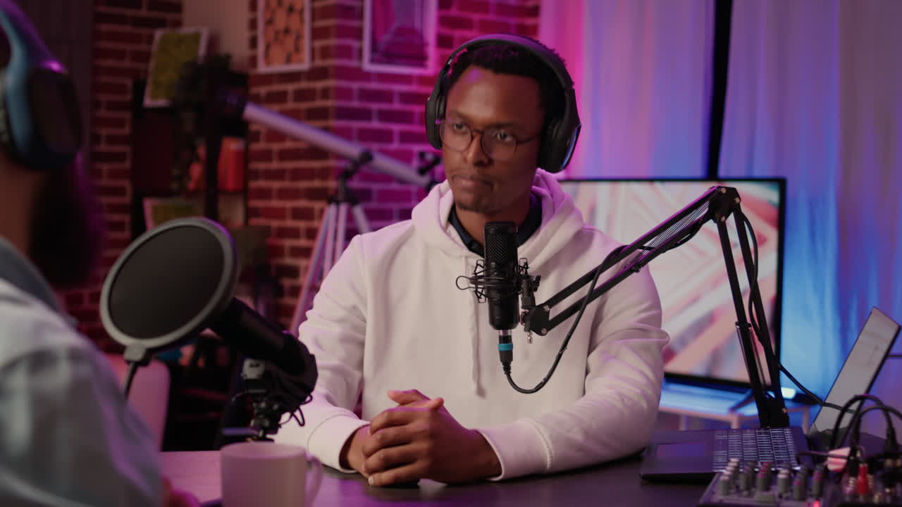 Internet radio host greeting guest doing fist bump hand gesture while recording podcast using digital video camera