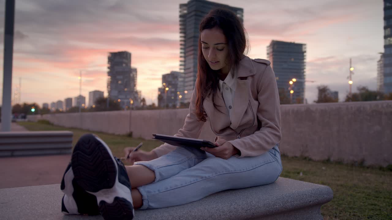 Mulher usando tablet ao ar livre ao pôr do sol em um cenário urbano.