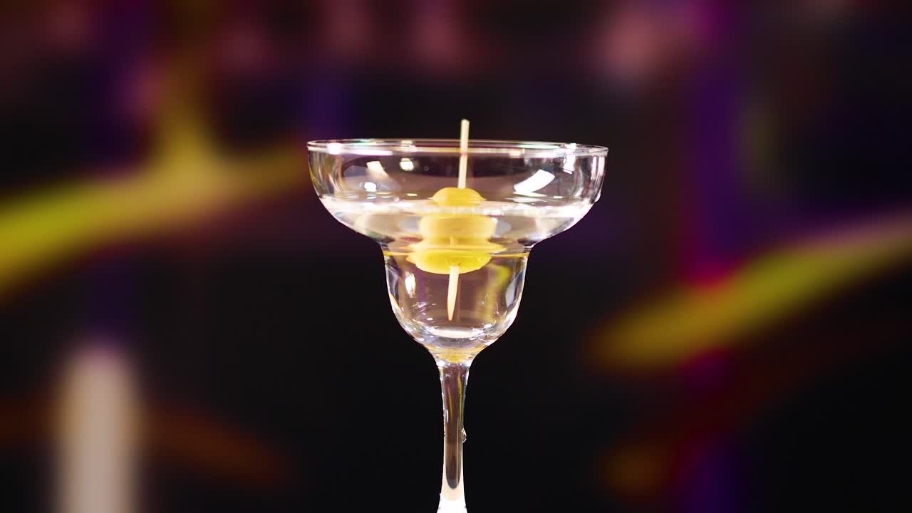Un bicchiere da martini con un'oliva come guarnizione su uno sfondo sfocato e colorato. Cattura un'atmosfera sofisticata e vibrante.