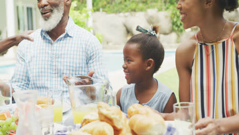 Happy-african-american-family-talking-and-having-breakfast-in-garden