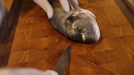 chef skilfully slicing around fish head on wooden chopping board