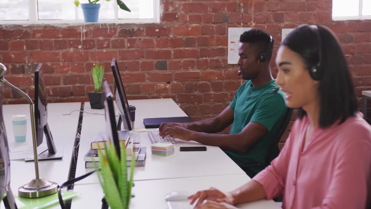 Diverse male and female business colleagues wearing headsets sitting at desks having video calls