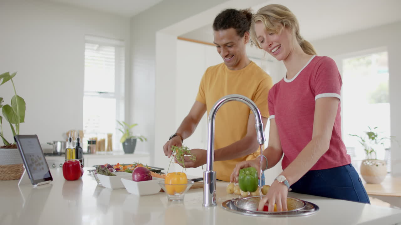 pareja feliz preparando y lavando verduras frescas en la cocina con tableta, cámara lenta