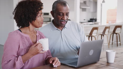 Senior-black-man-and-his-middle-aged-daughter-using-a-laptop-and-laughing-together-at-home,-close-up