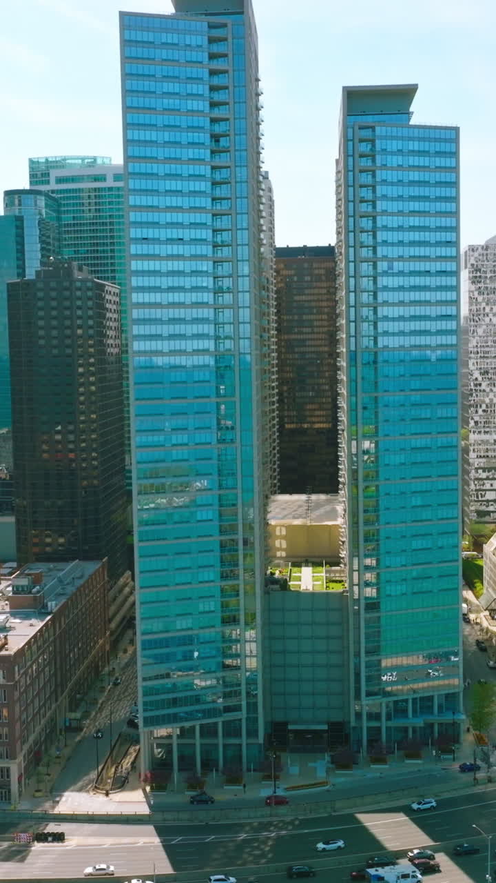 Blue skies and turquoise waters reflecting in the mirror windows of skyscrapers. Multi-line road with busy traffic near the buildings. Vertical video