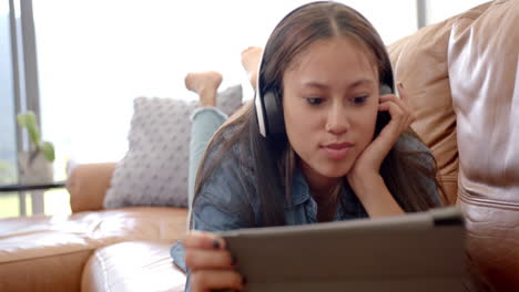 watching video on tablet, young asian woman wearing headphones on couch