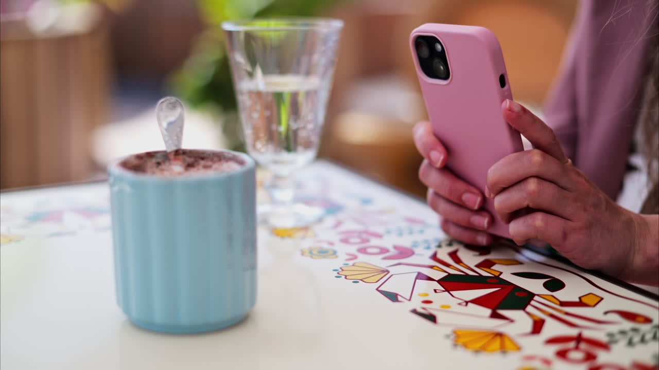 Close up of hot chocolate in a blue cup with a woman holding her phone at a white table