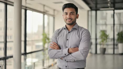 confident young professional standing with crossed arms, radiating leadership and success in sleek modern office environment, expressing positive entrepreneurial spirit