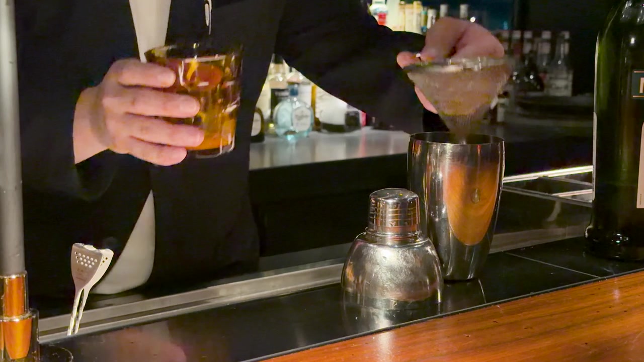 Un barista in abito filtra un cocktail attraverso un colino a maglie fini a Kanazawa