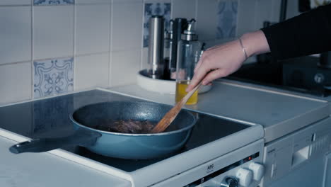 cooking meat in a pan on a stove in white kitchen