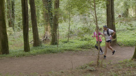 man and woman in sportswear running on trail in forest