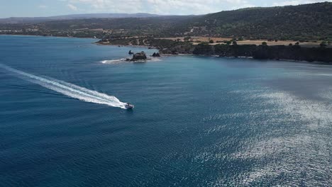 Speedboat-passing-Akamas-peninsula-in-Chrysochou-Bay,-aerial-tracking