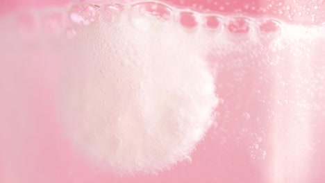 view of a blurred effervescent tablet dissolving in water with a pink background