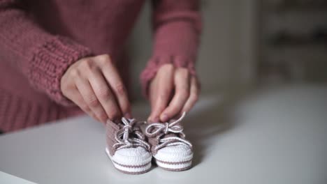 mother hands playing with pink baby booties. knitting clothes for baby