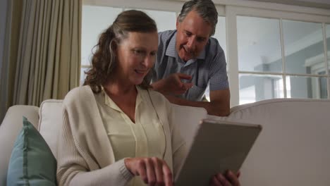 happy senior caucasian couple in living room using tablet and talking