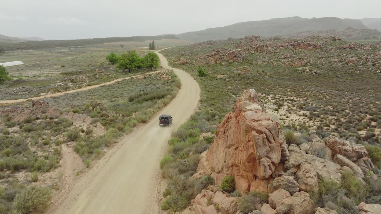 드론이 서서히 길 으로 올라가서 검은색 오프 로드 차량이 남아프리카 공화국의 세더버그 야생 지역에서 운전하는 곳 - 배경에는 바위 산을 볼 수 있습니다.